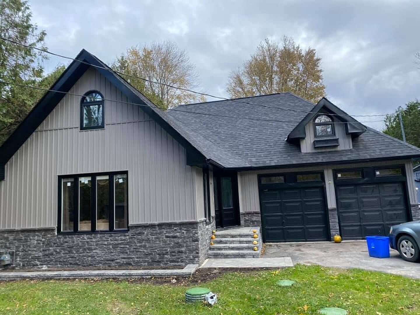 Finished taupe board-and-batten home exterior with dark windows, garage doors, and stone base.