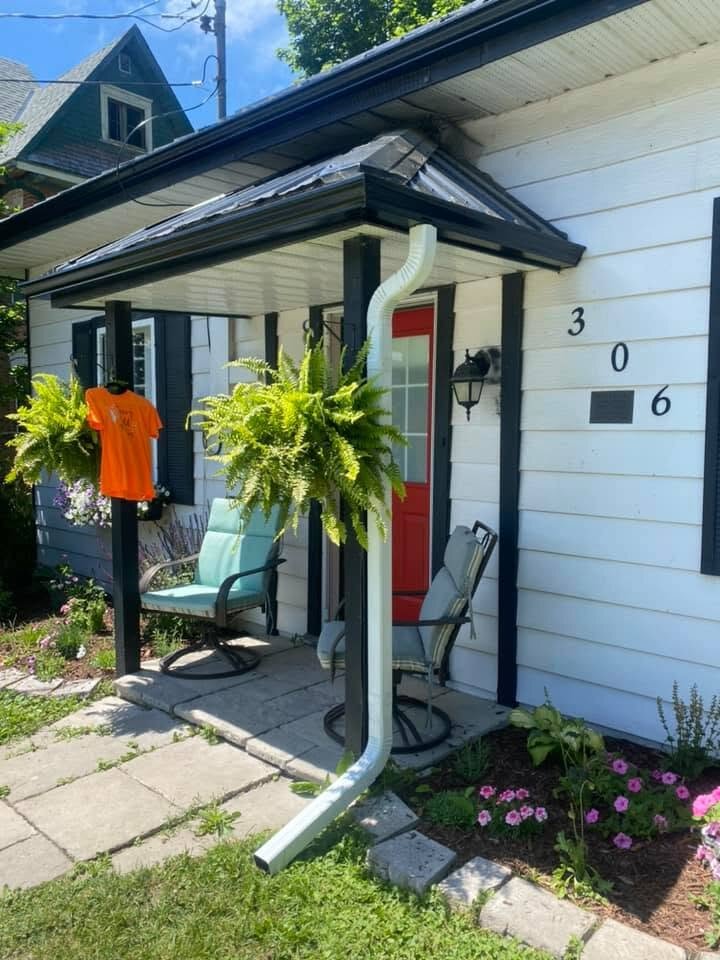 Black eavestrough and downspout on a white-sided home with a covered porch.