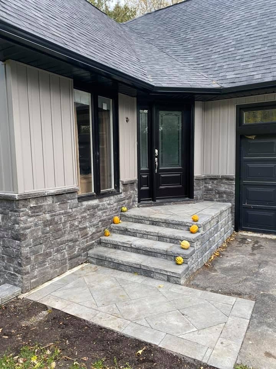 Front entry with stone steps, dark trim, and taupe board-and-batten siding.