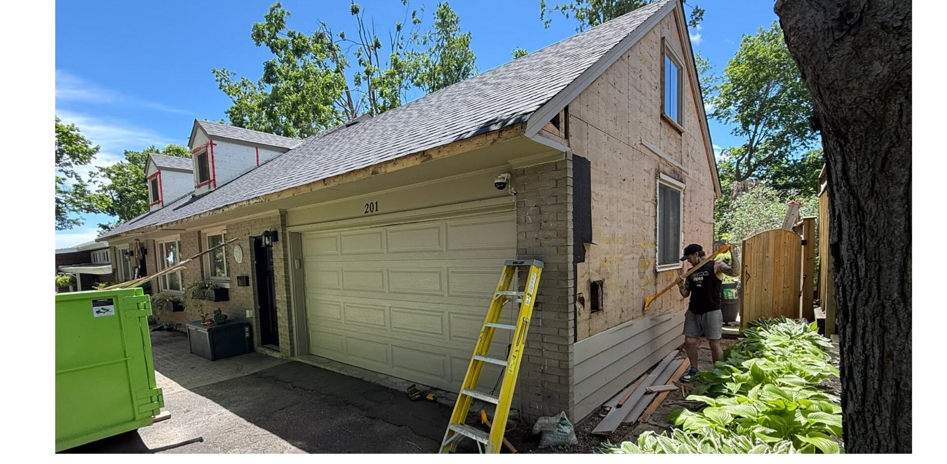 Garage during exterior work with wall sheathing exposed and a ladder at the roofline.