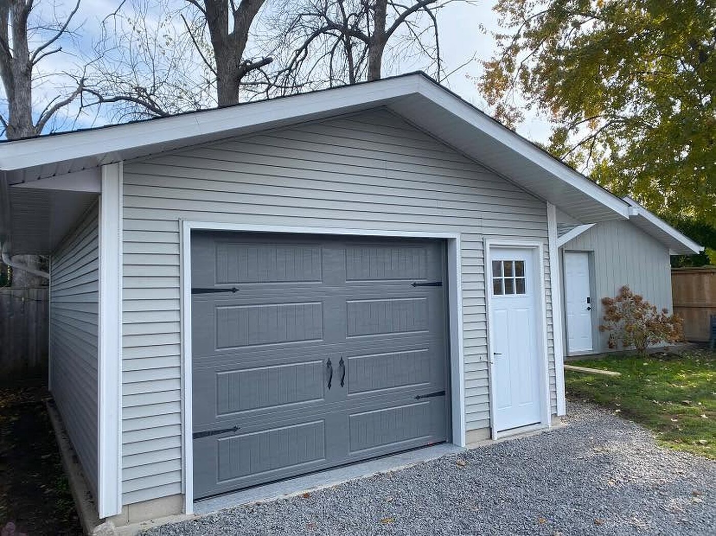 Detached garage with light siding, a grey overhead door, and a finished roof edge.