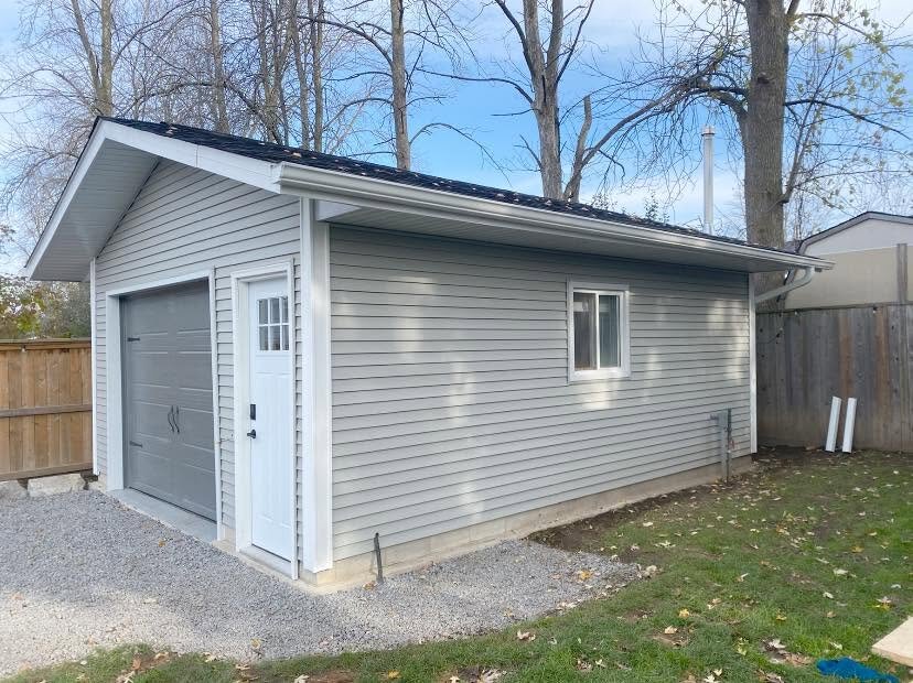 Detached garage with light siding, white eavestrough, and a grey door.
