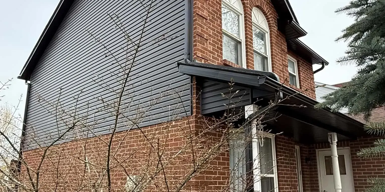 Finished dark siding, soffit, fascia, and eavestrough work on a brick home.