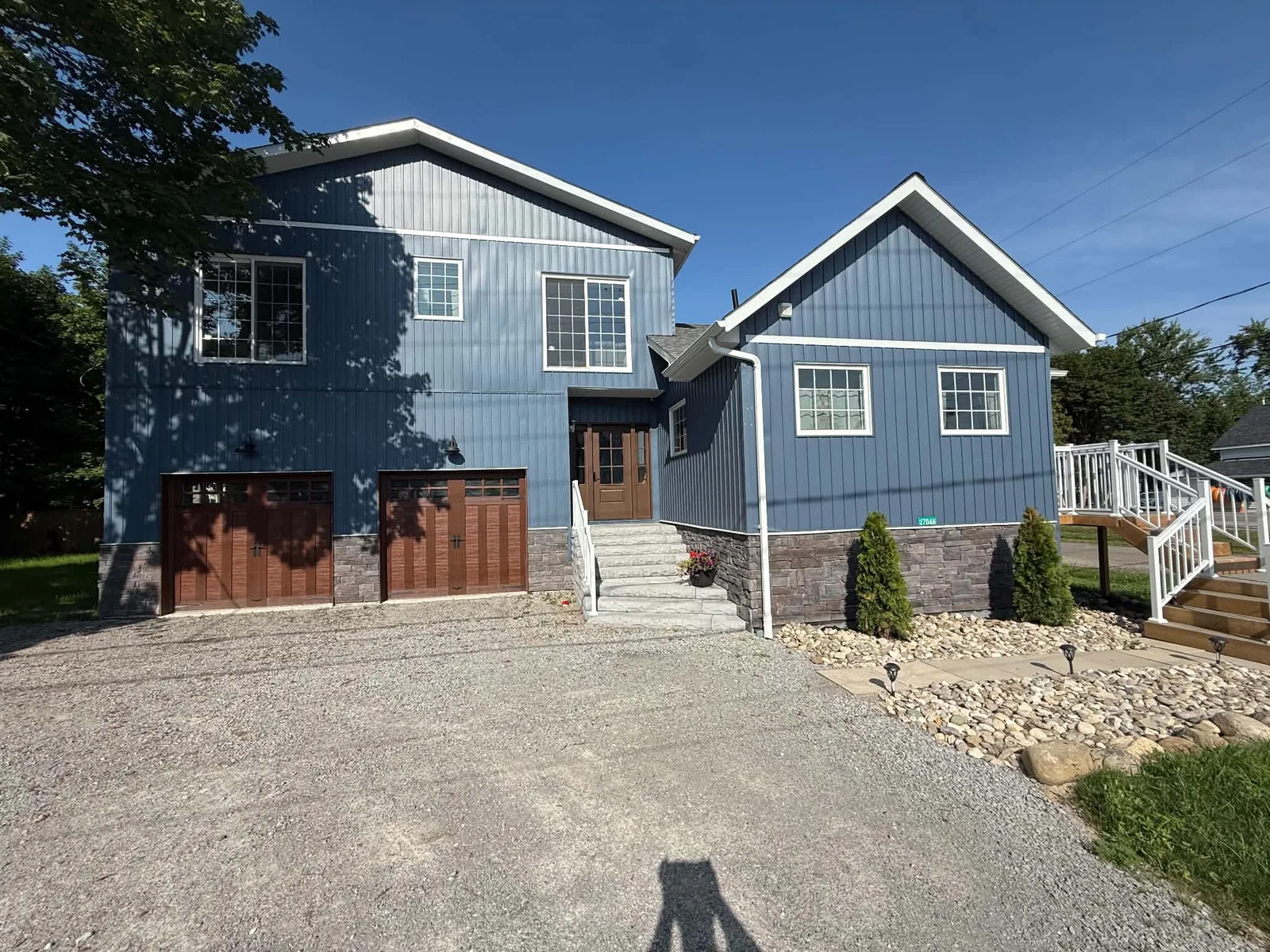Driveway view of a completed blue board-and-batten home with dark garage trim.