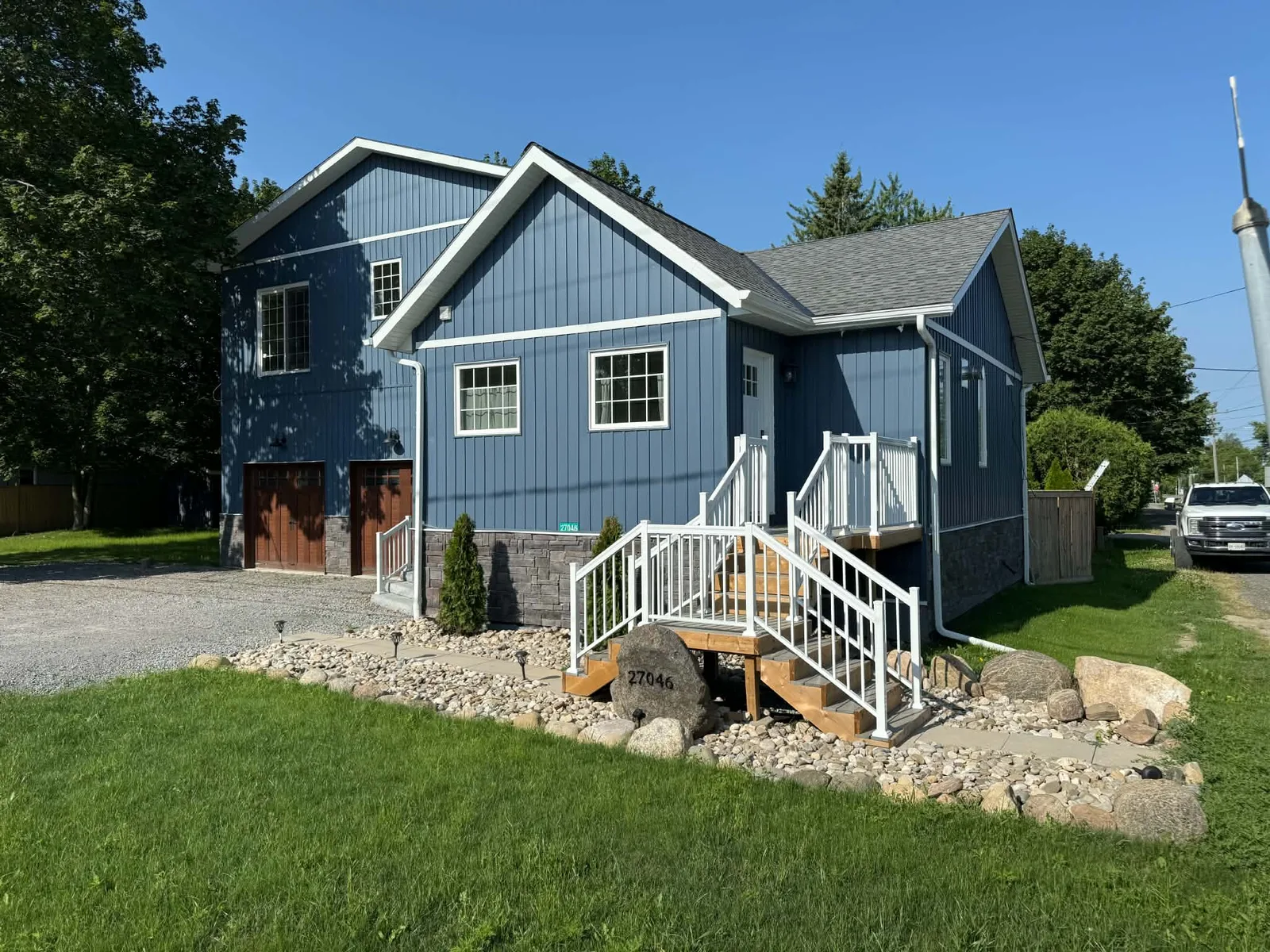 Finished blue board-and-batten home viewed across the front landscaping.