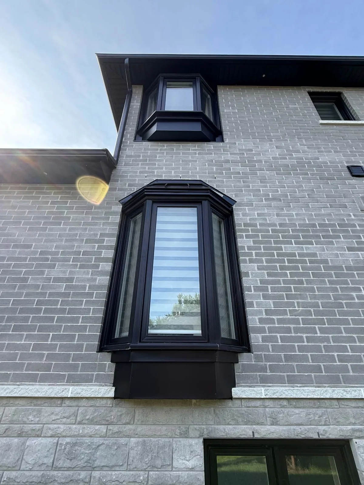 Close view of a brick bay window finished with dark cladding and trim.