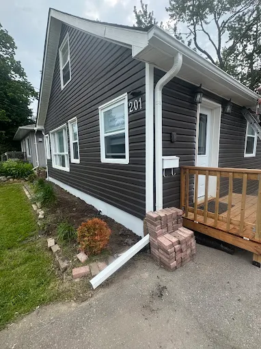 Rear angle of a dark-sided bungalow with white eavestrough and downspout.