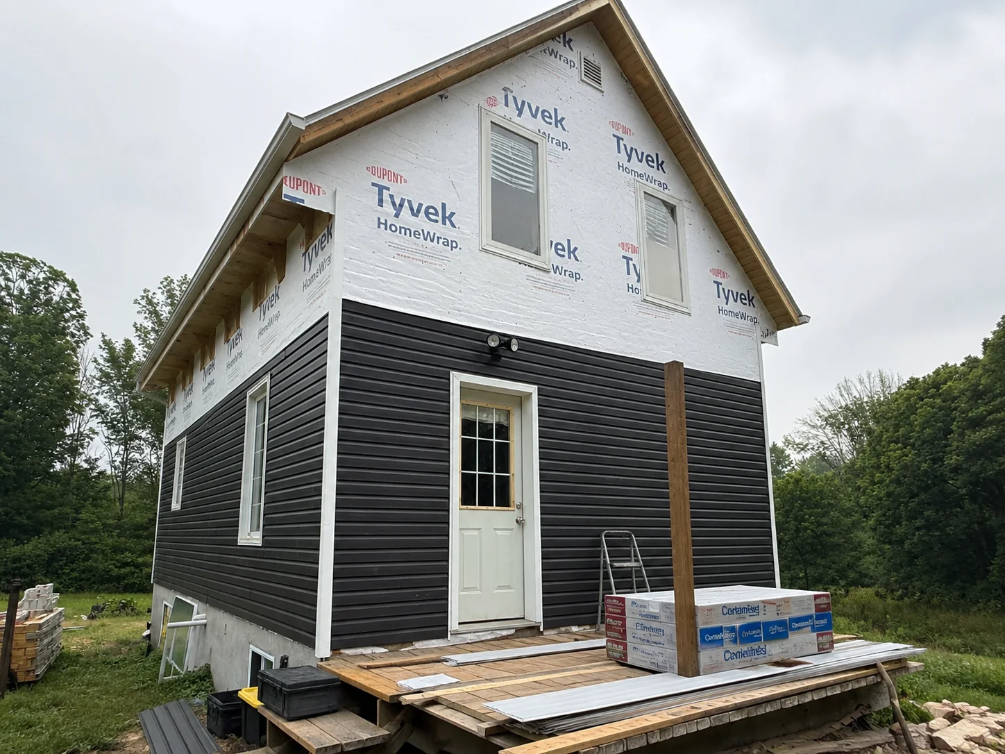 Deck elevation with lower dark siding installed and the upper wall still wrapped.