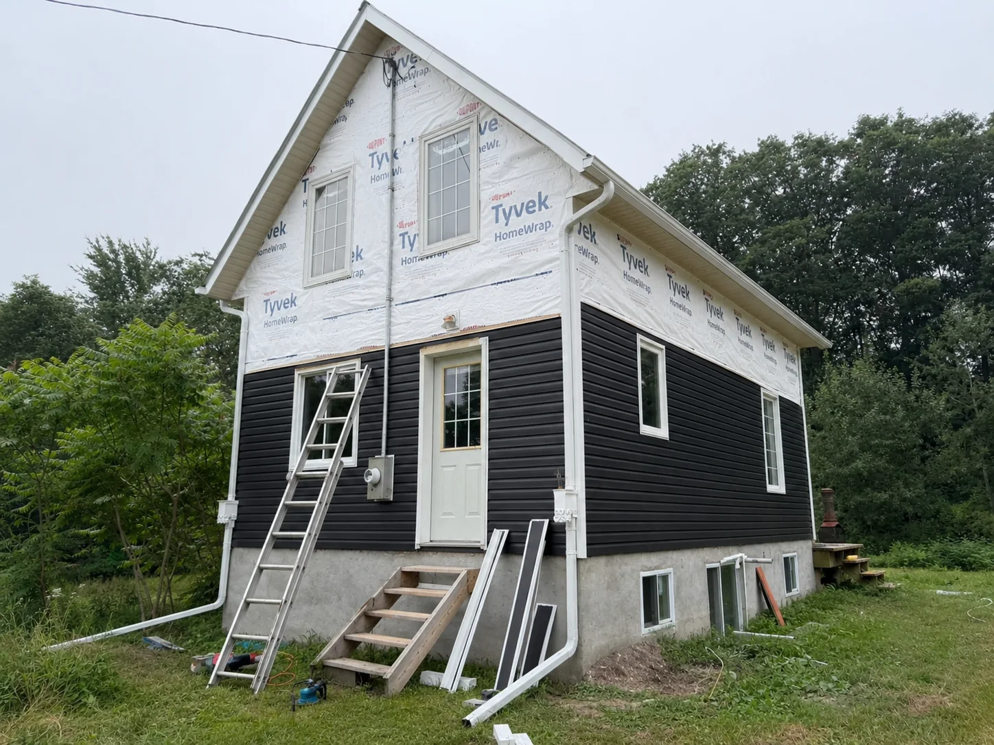 Main elevation wrapped for weather protection with dark siding installed on the lower walls.