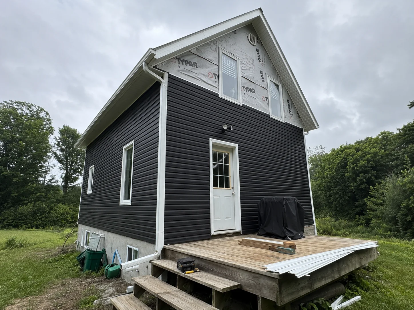 Dark siding installed across the lower elevation while the upper gable remains wrapped.
