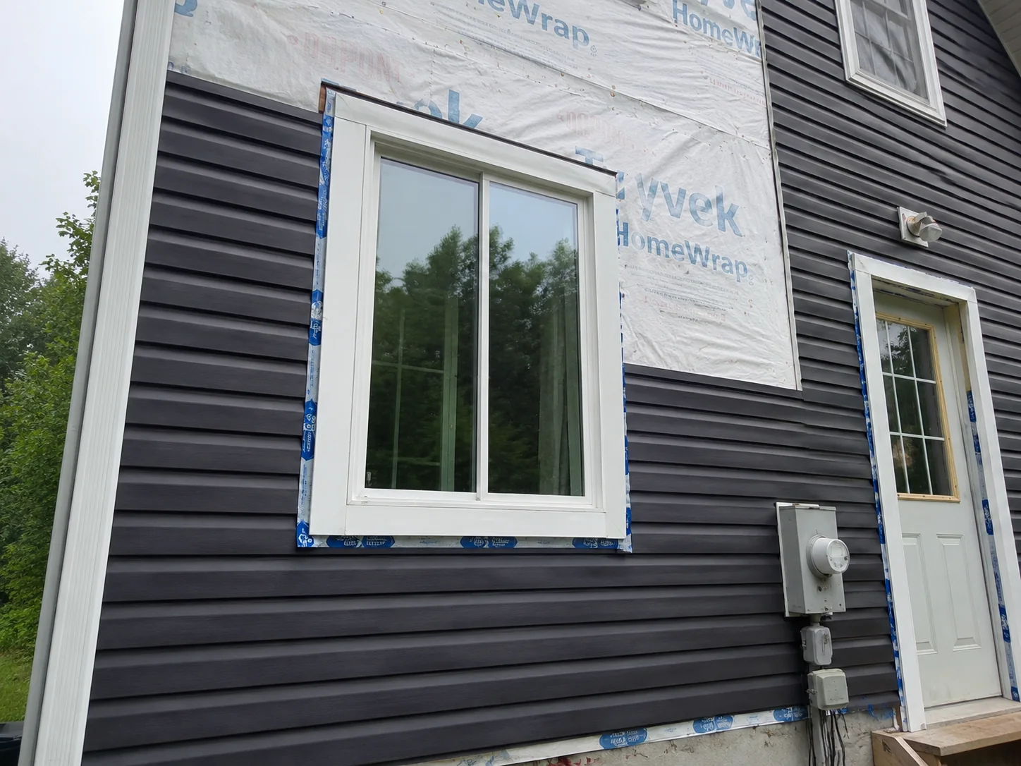 Close view of dark siding meeting a wrapped wall around a white window and door.