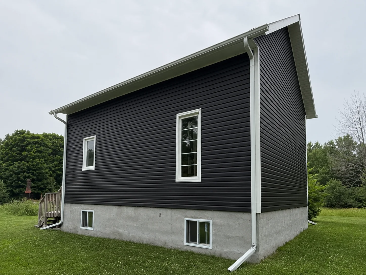 Long side elevation finished with dark horizontal siding and white window trim.