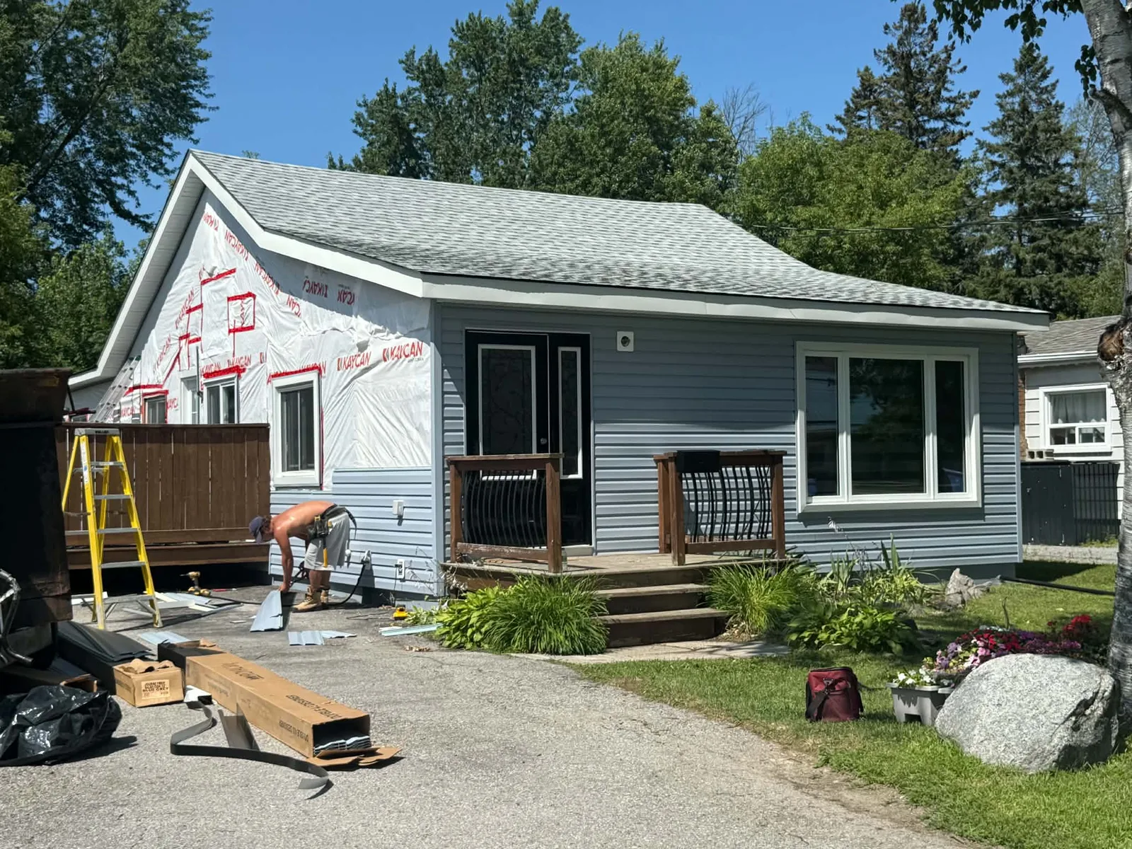 Light-grey horizontal siding being installed across the front of a bungalow.