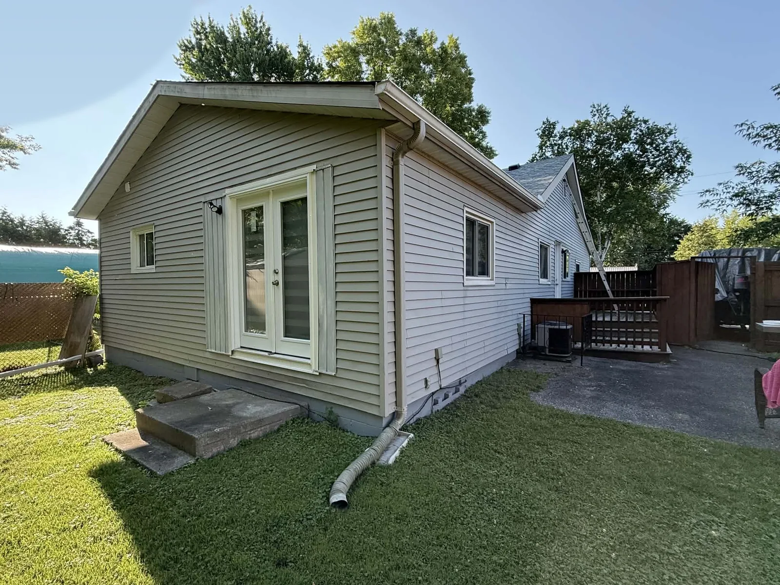 Rear corner of a bungalow with finished light-grey siding, white trim, and a downspout.