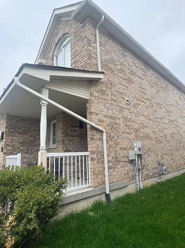 White eavestrough and downspout installed along a brick house roofline.