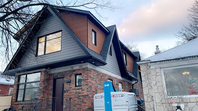 Wide view of a brick home finished with dark grey siding and dark trim.