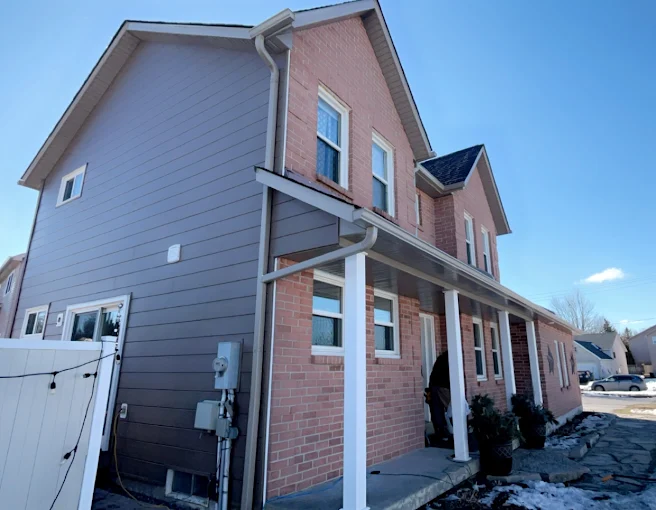 Brick two-storey home with finished grey horizontal siding and dark trim.