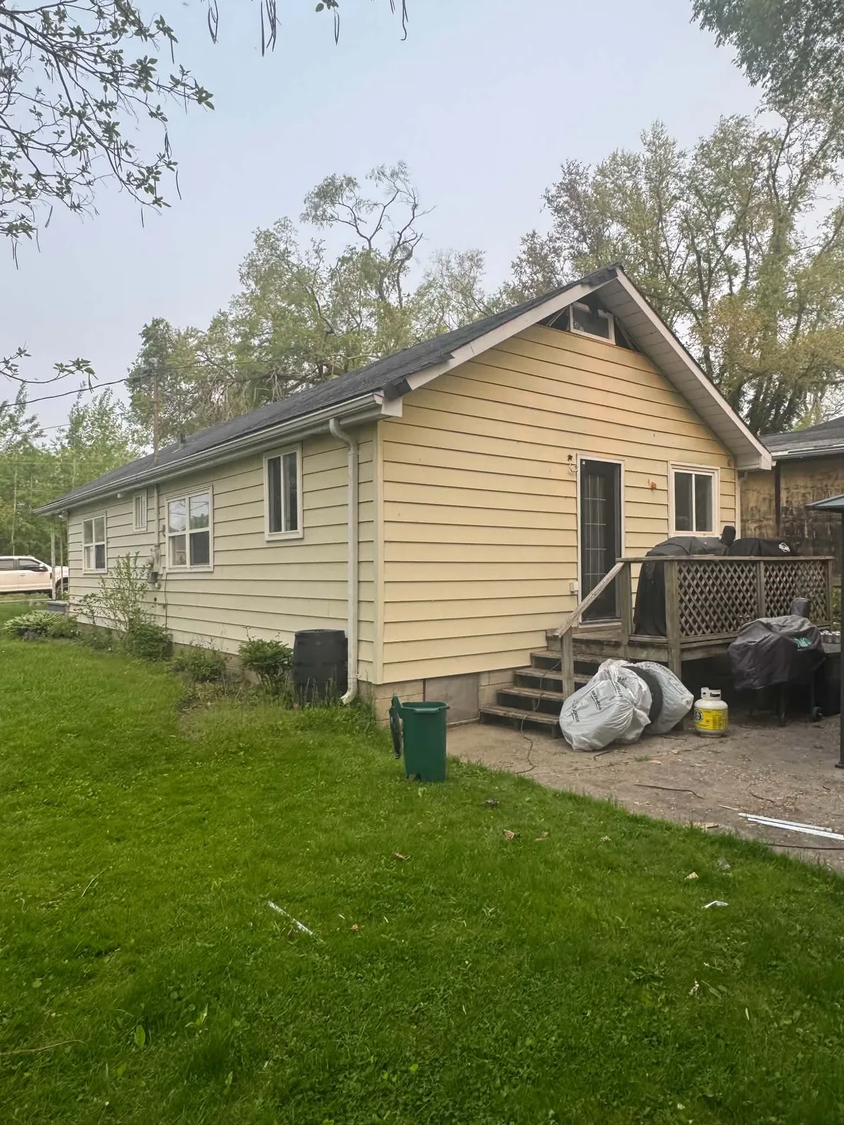 Tan horizontal siding on the rear and side of a cottage before replacement.