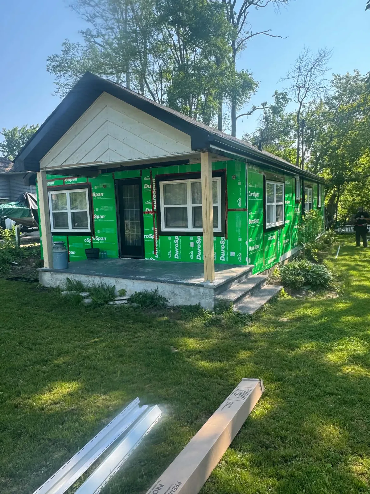 Front of a cottage covered in green housewrap during siding replacement.