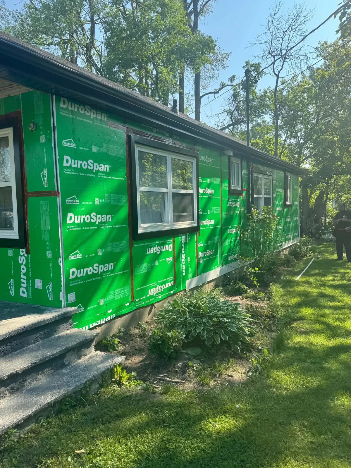Side wall covered in green housewrap during the cottage siding project.