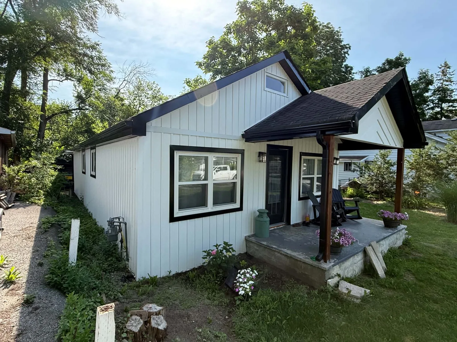 Front and side of a cottage finished in white siding with black roofline trim.