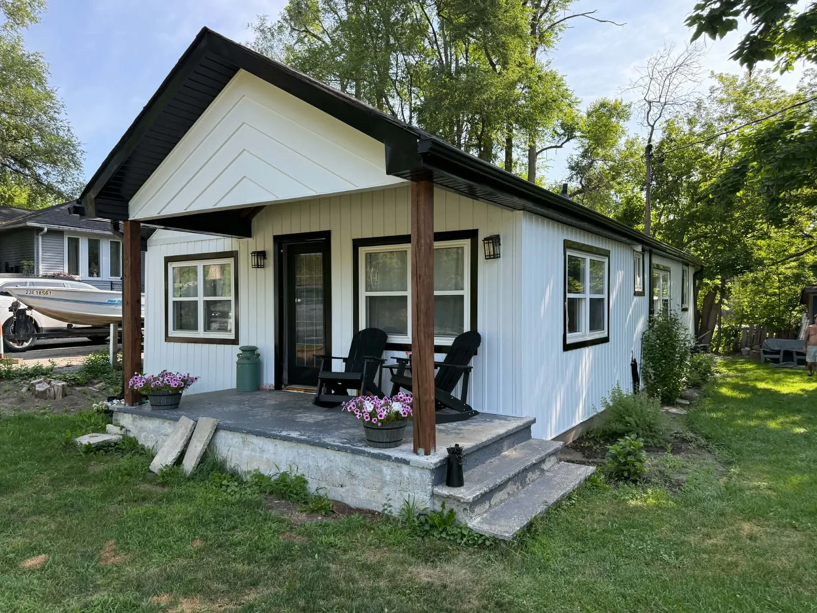 Finished cottage with white vertical siding, black trim, and timber porch posts.