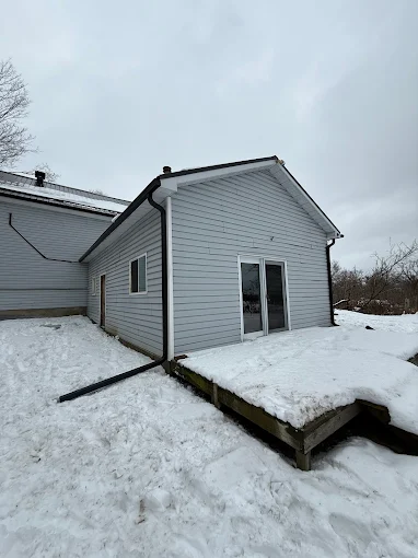 Side view of white siding with a black downspout and roofline trim.