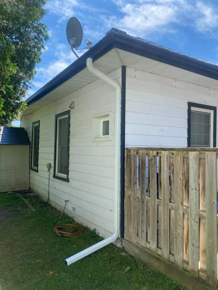 Rear addition with white siding and a downspout beside a wood fence.