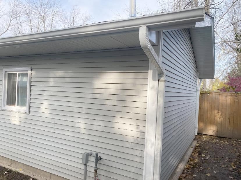 Light siding meeting soffit, fascia, eavestrough, and a downspout at a home corner.